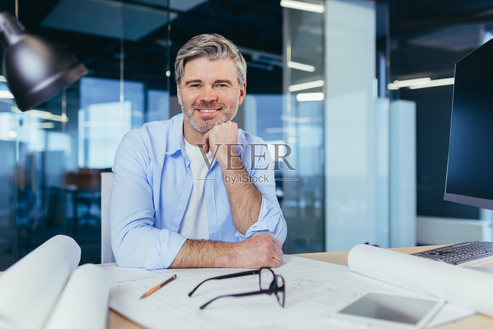 经验丰富的灰发设计师建筑师，微笑着看着摄像机，男子在新办公中心的建筑投影仪照片摄影图片