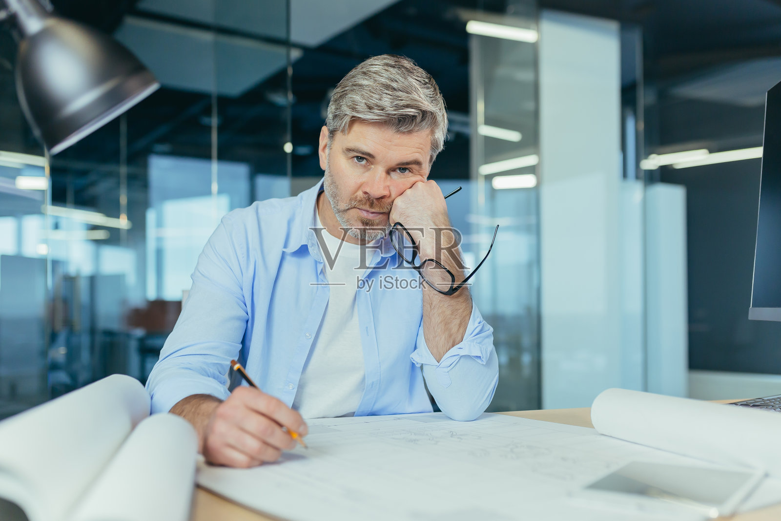 想想高级男建筑师正在做一个重要的项目。桌子旁有一台电脑和一幅画照片摄影图片