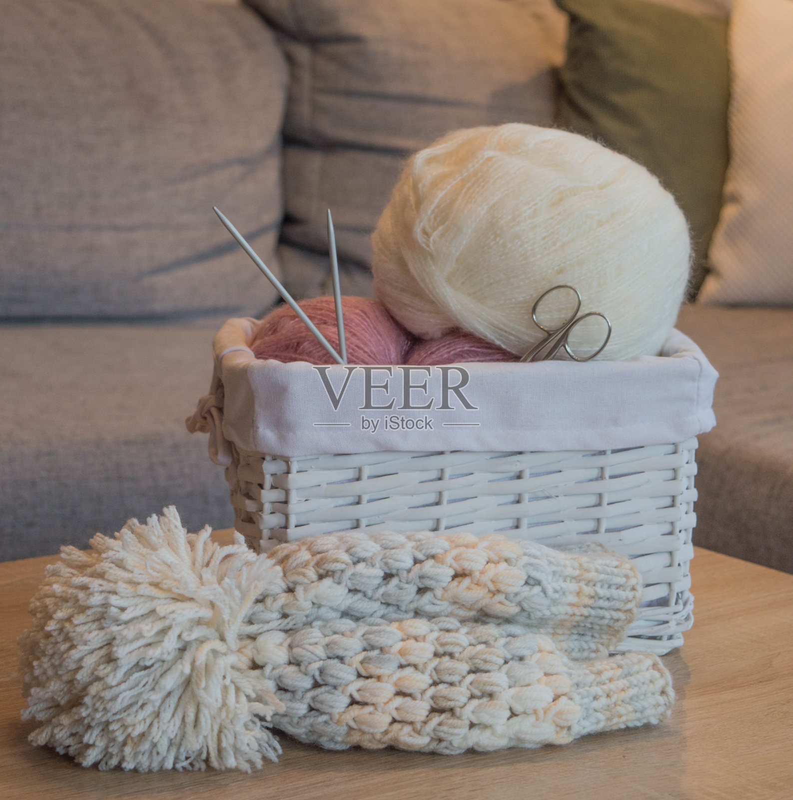 粉红色和白色的羊毛球在一个白色的篮子里，编织针和编织的帽子照片摄影图片