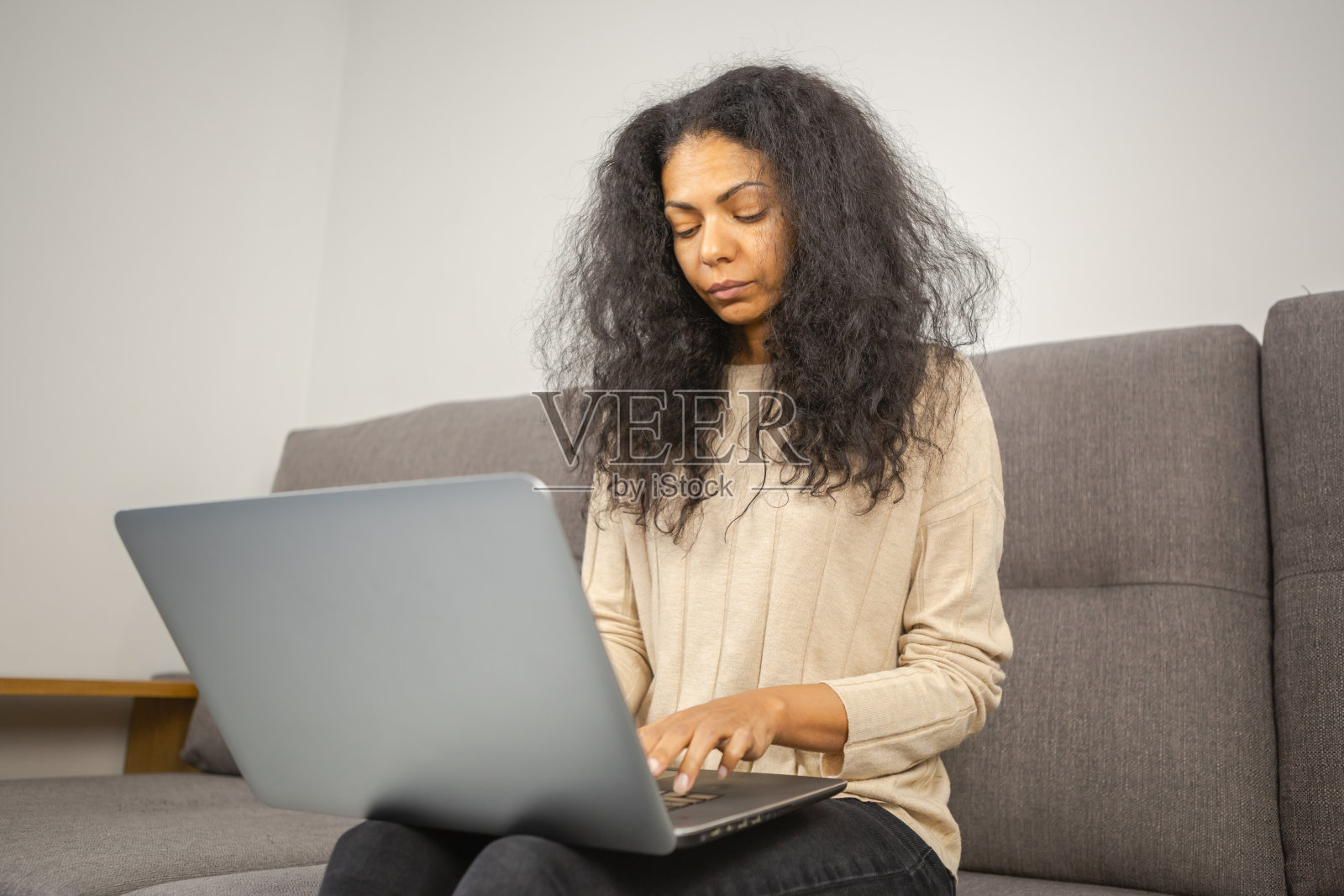 年轻漂亮的黑人女性在电脑上工作。非洲女性坐在客厅的沙发上用笔记本电脑进行远程工作。自由职业者在家里用笔记本工作照片摄影图片