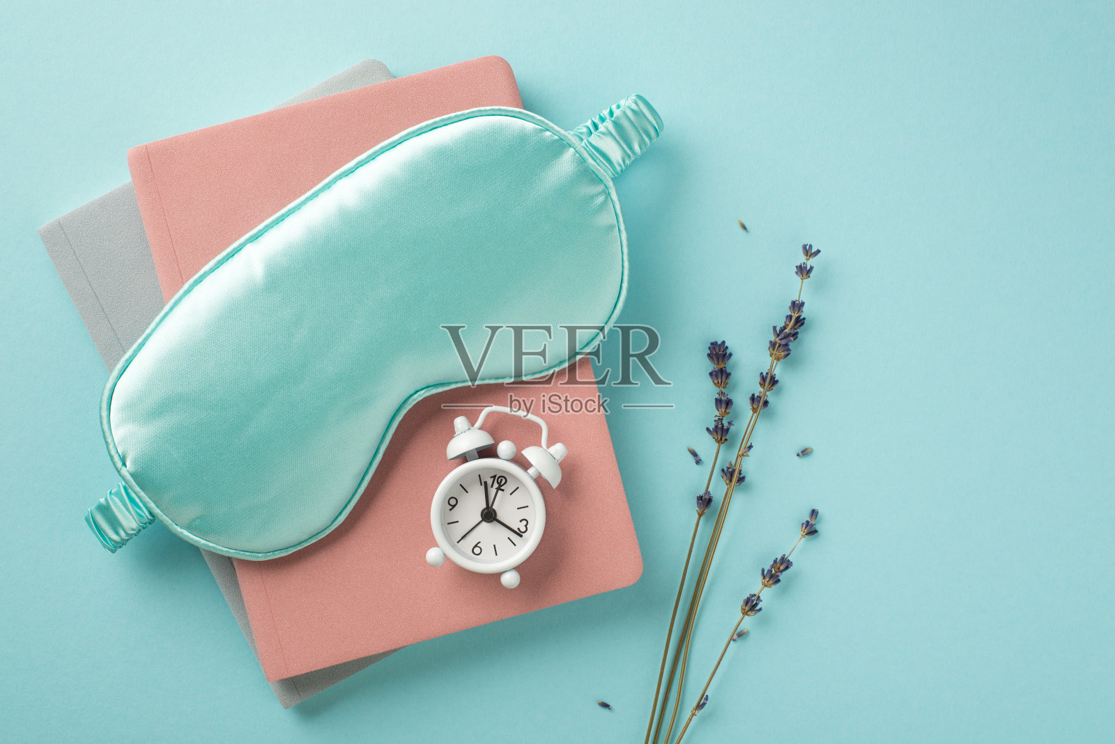 俯视图照片的蓝色丝绸睡眠面具小白色闹钟的规划者和小枝薰衣草在孤立的柔和的蓝色背景与copyspace照片摄影图片