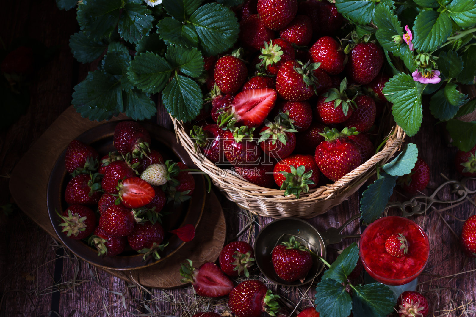 成熟的新鲜草莓在柳条筐在黑色的背景与绿色的叶子和粉红色的花在草莓植株上照片摄影图片