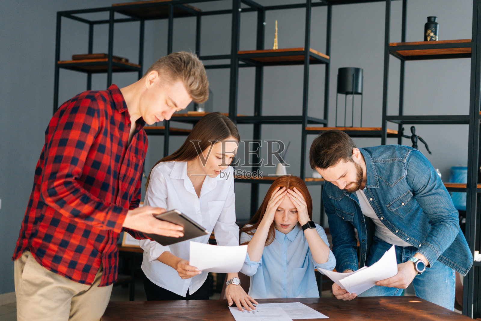 疲惫的年轻女商人坐在桌子旁，多种族的同事摇晃着文件。照片摄影图片