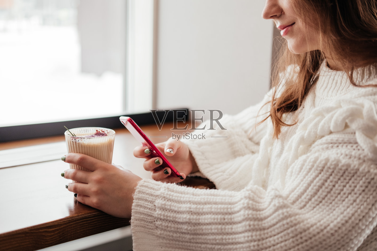 年轻女子在咖啡厅用手机喝咖啡。白人女孩在室内穿毛衣。照片摄影图片