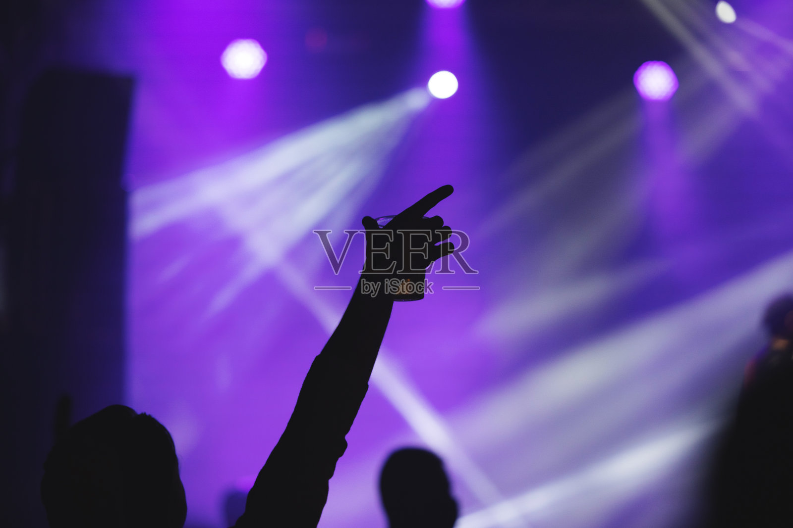 人们在享受一场音乐会的概念时，人们的剪影在听音乐时举起他们的手，集中在前景上，模糊的紫色背景照片摄影图片