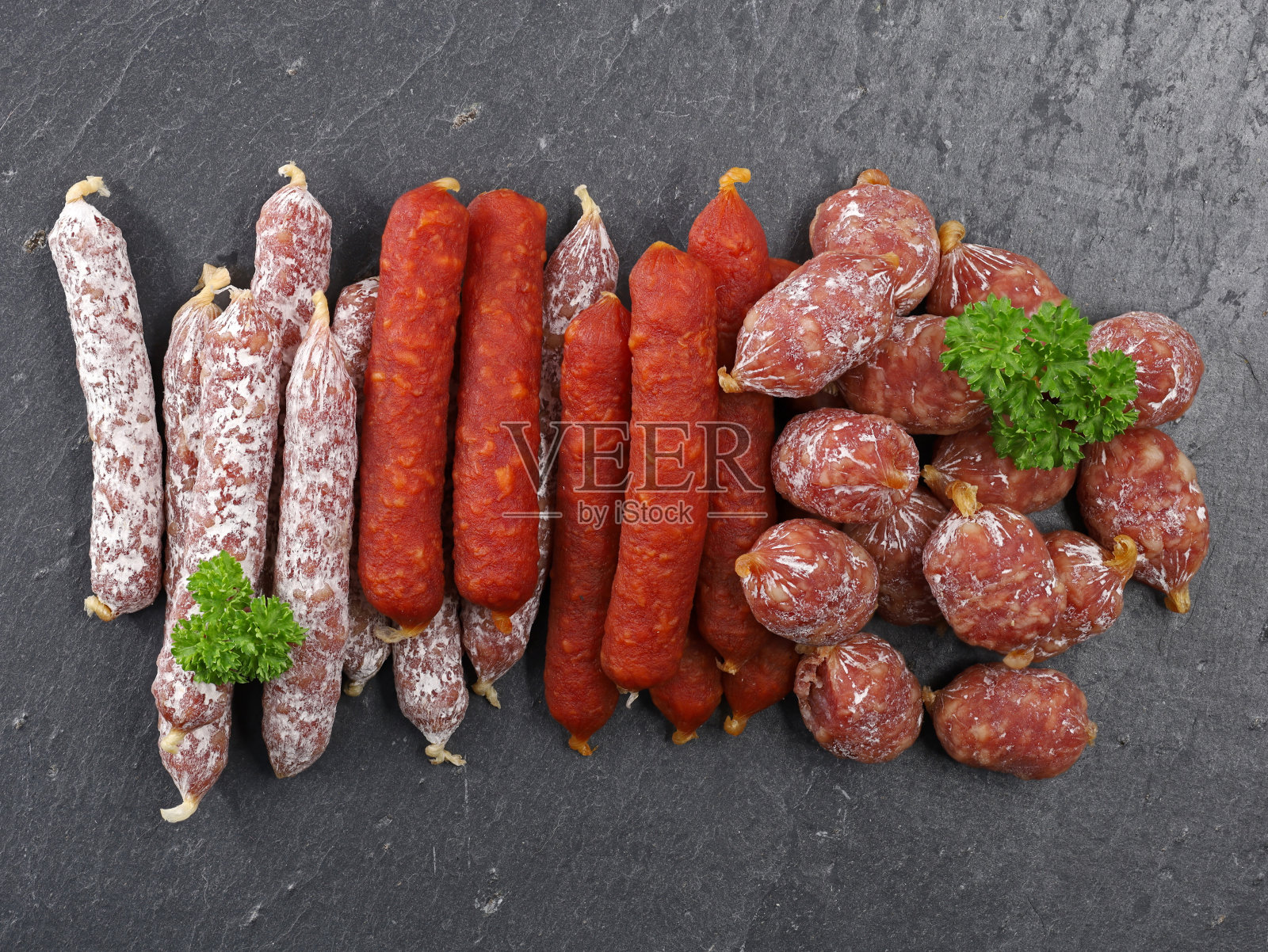 各种各样的肉类小吃组合，在黑色石板板上俯视图几个风干的迷你香肠照片摄影图片