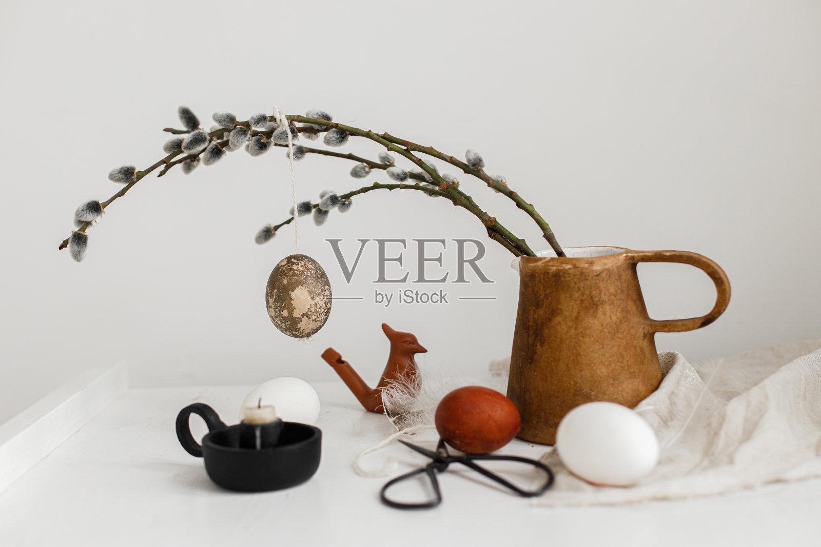 复活节乡村静物。天然的复活节彩蛋挂在柳枝上，蜡烛，木桌上的羽毛。简单时尚的复活节装饰在餐桌上的美学。复活节快乐!照片摄影图片