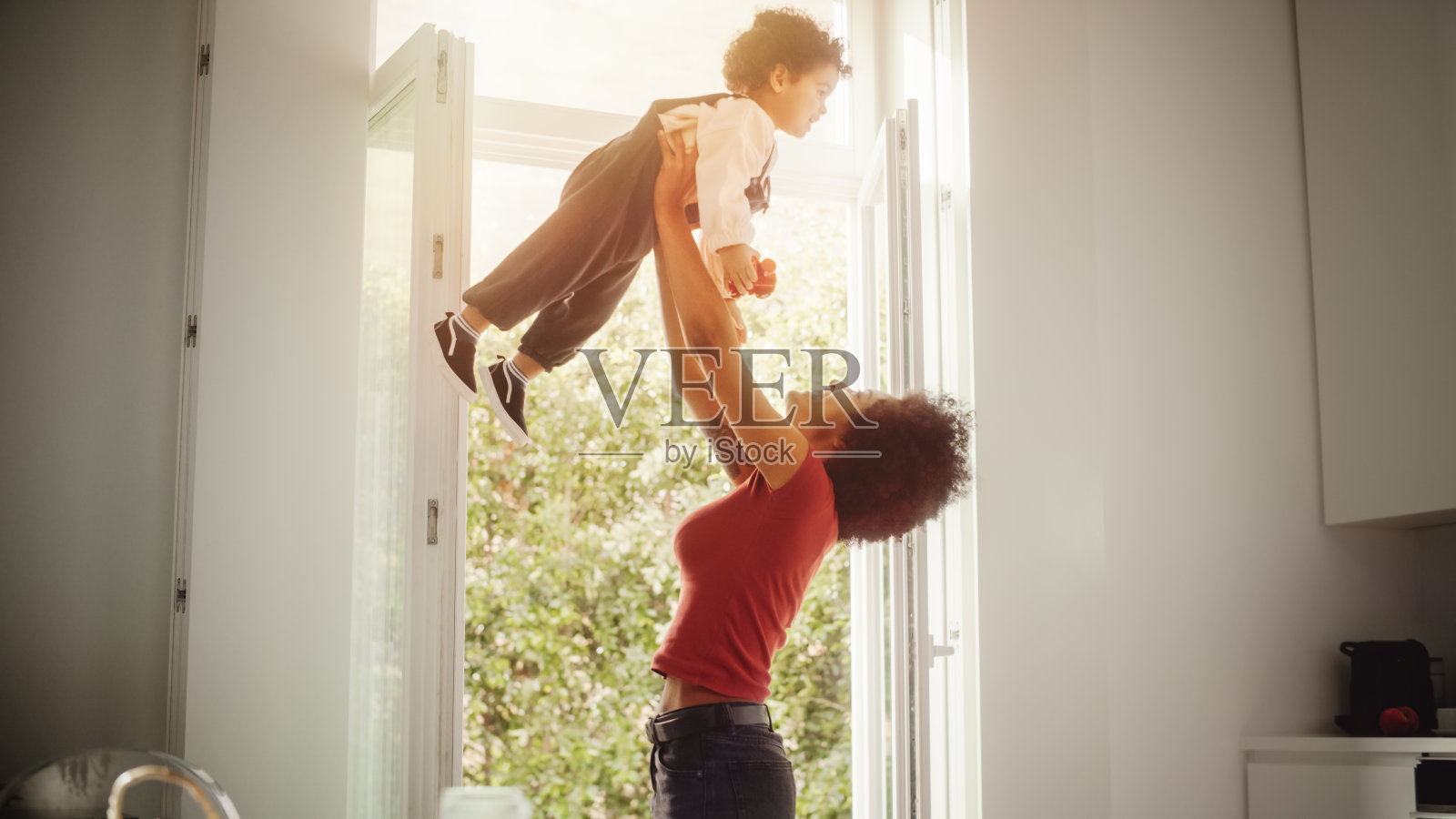 快乐的母亲抱着可爱的小男孩，玩，有乐趣在现代家庭客厅。黑人女性将蹒跚学步的孩子举到空中。童年、新生活、亲子观念。照片摄影图片