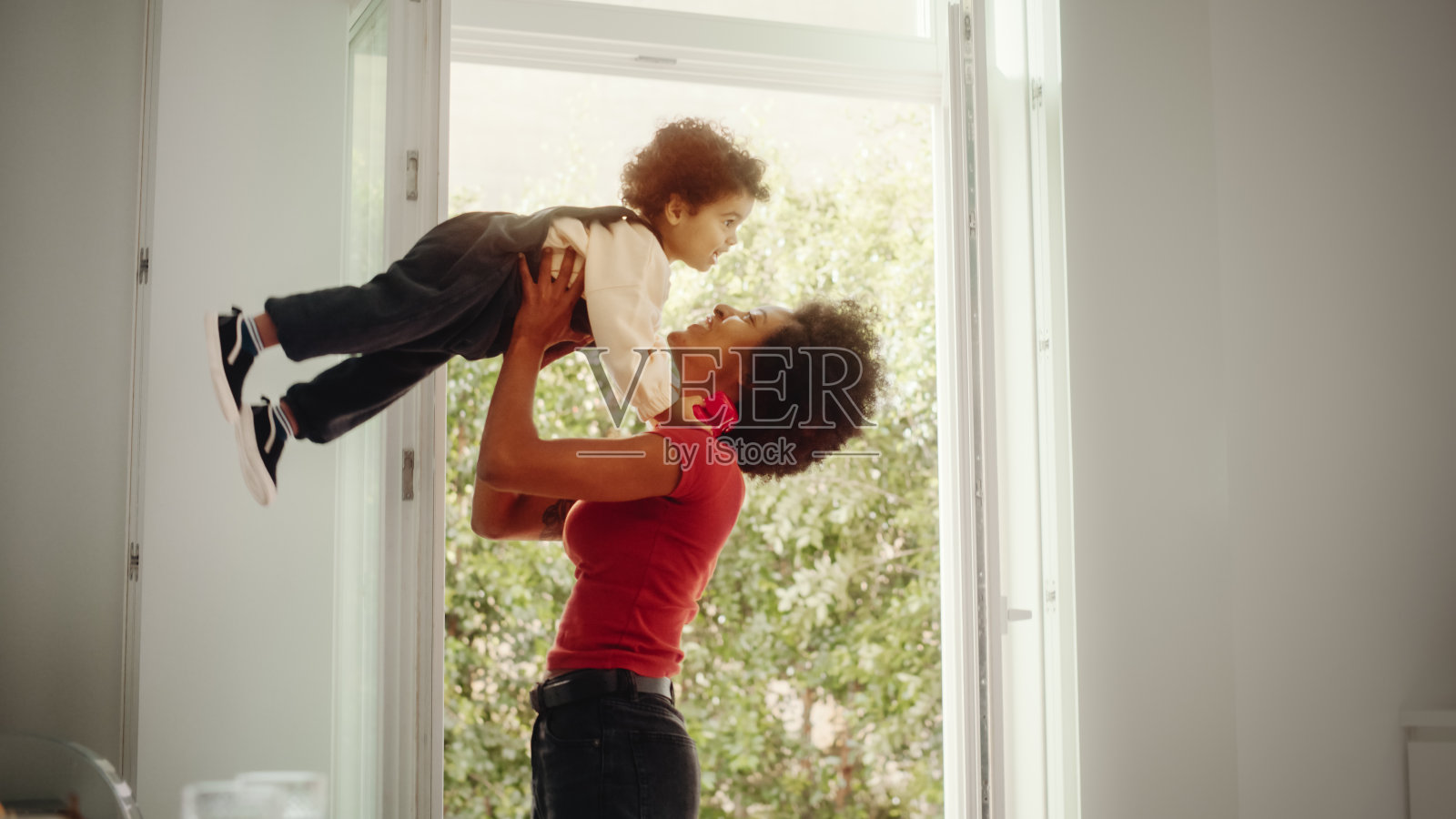 快乐的母亲抱着可爱的小男孩，玩，有乐趣在现代家庭客厅。黑人女性将蹒跚学步的孩子举到空中。童年、新生活、亲子观念。照片摄影图片