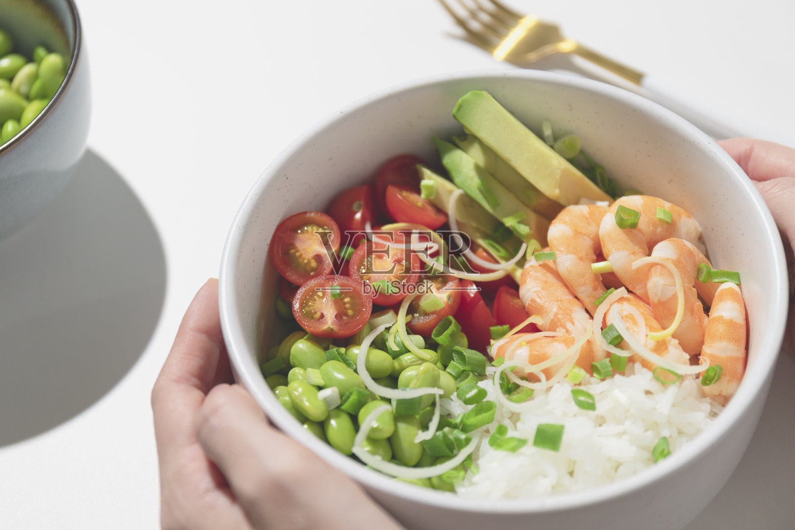 女人拿着一个poke碗，碗里有红色的虾、米饭、西红柿和毛豆。照片摄影图片