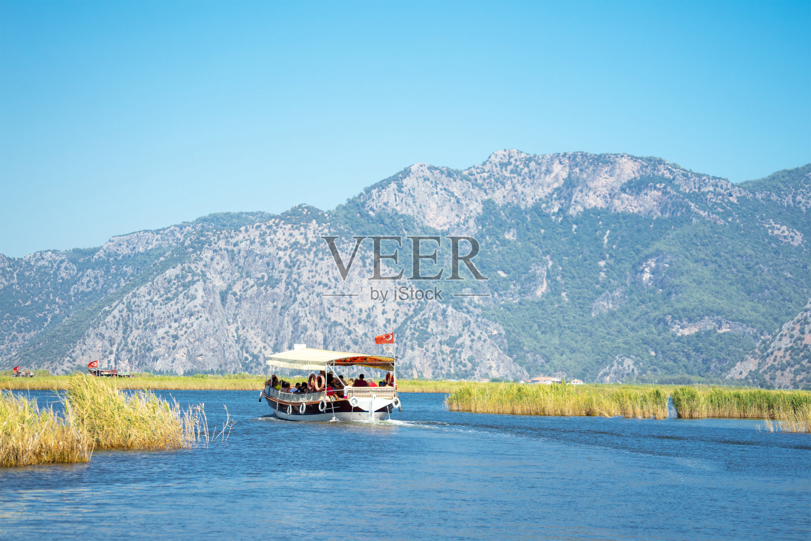 在土耳其西南海岸的马尔马里斯和费提耶地区之间的穆格拉省(Mugla Province)，游客游船在达利扬河(Dalyan River)上，靠近岩石，岩石上有吕西亚人的坟墓照片摄影图片