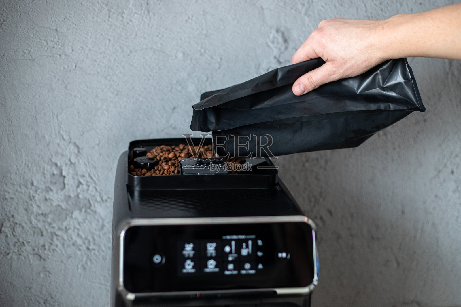 一个男人拿着黑色咖啡袋的手把咖啡豆倒进了咖啡机照片摄影图片