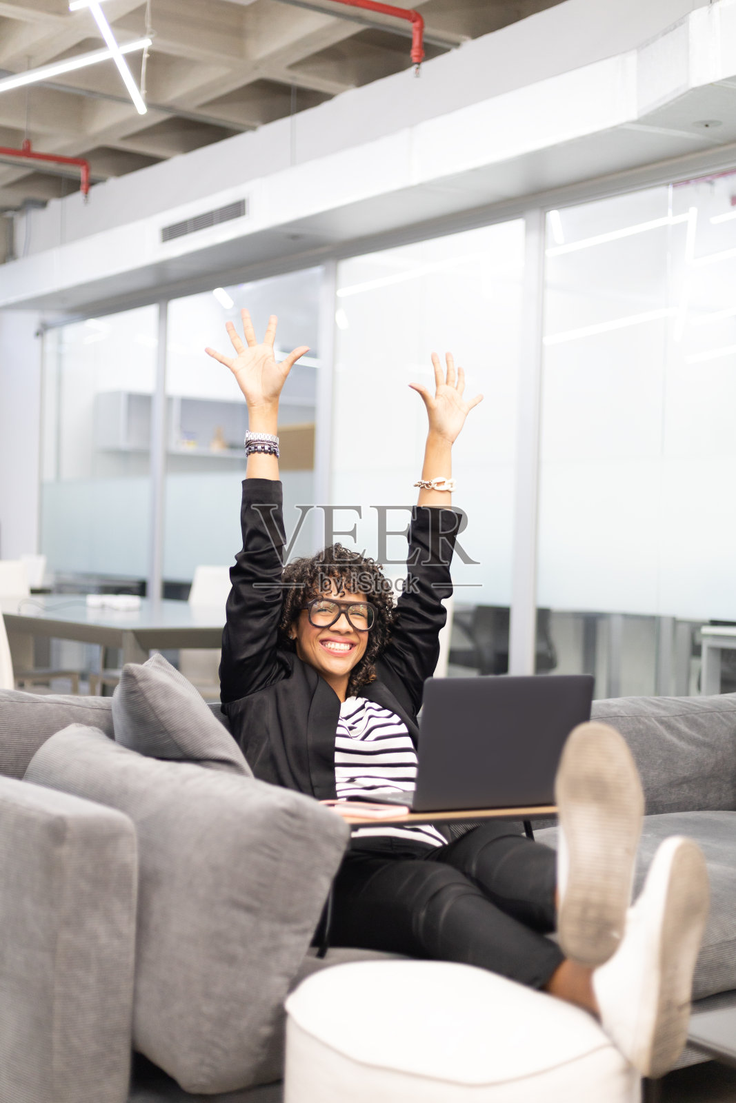 加勒比海卷曲的年轻女子在沙发上愉快地工作着，手里拿着一台笔记本电脑照片摄影图片