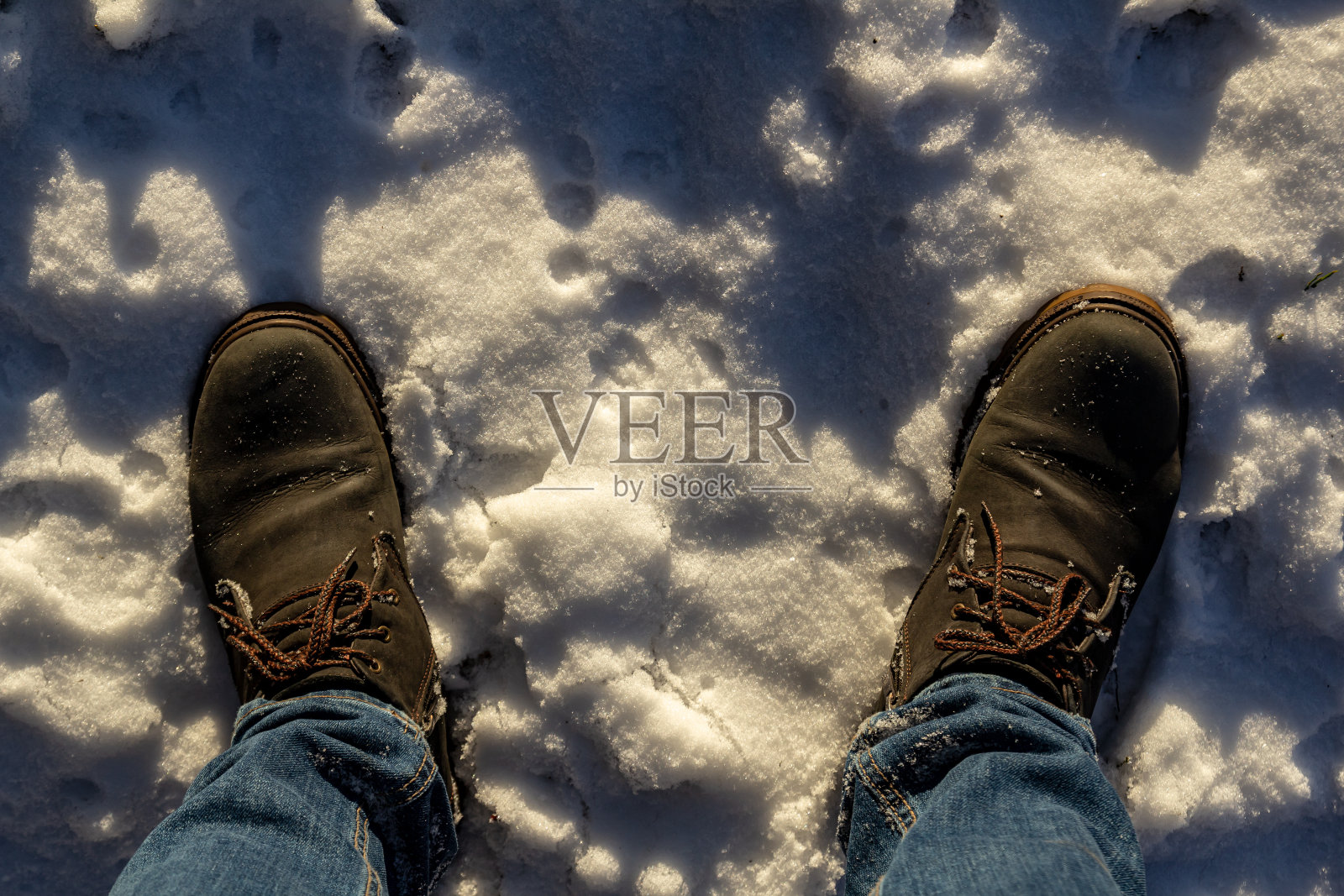 脚穿着蓝色温暖的靴子踩在雪白的雪地上。俯视图照片摄影图片