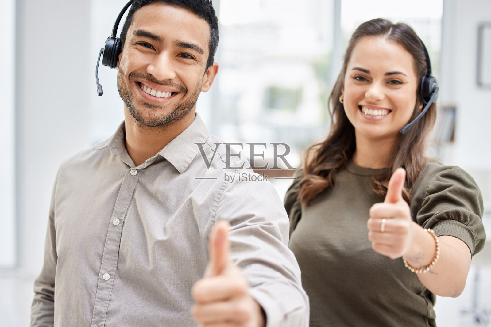 裁掉的肖像的两个年轻的呼叫中心的代理人给大拇指，而站在办公室照片摄影图片