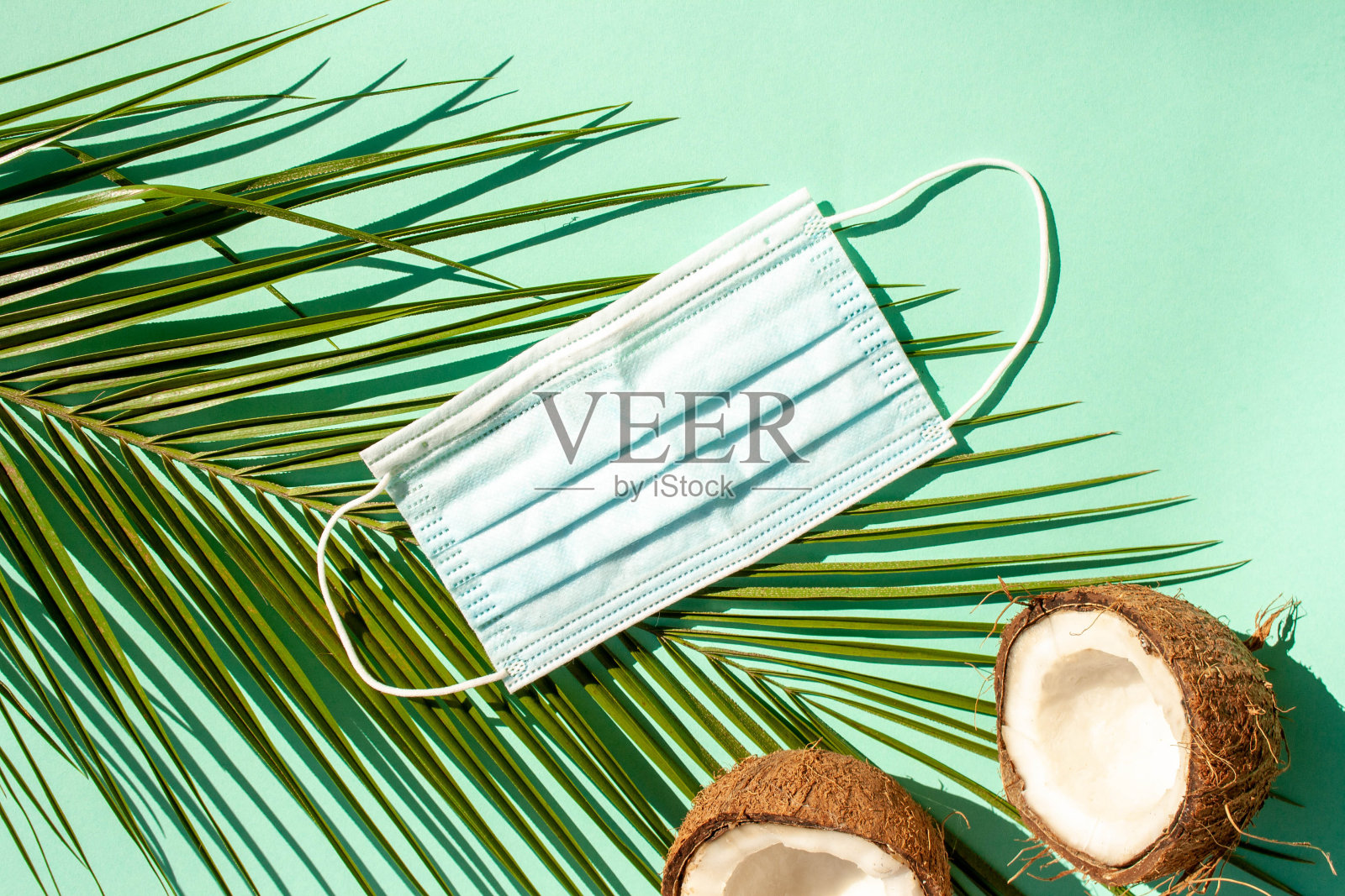 医用防护口罩，蓝色背景的棕榈叶和椰子。流行病期间的度假概念照片摄影图片