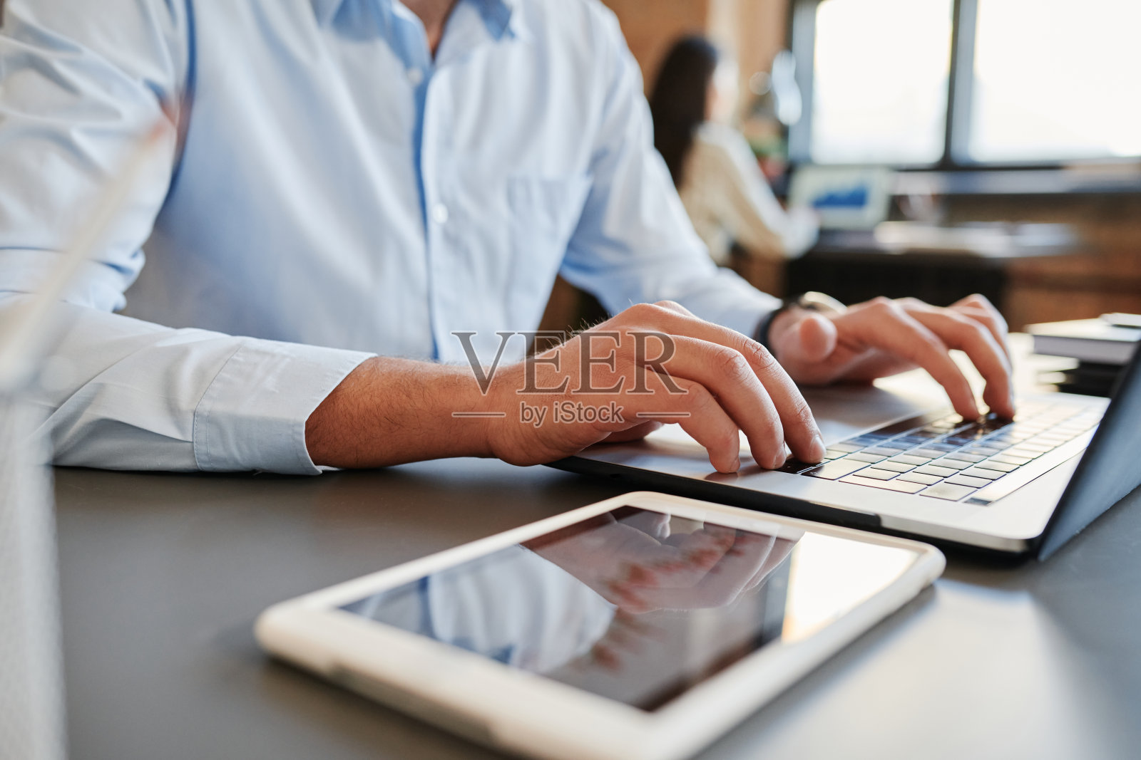 在办公室里坐在桌前用笔记本电脑工作的，穿着蓝色衬衫的，无法辨认的男士中景特写镜头照片摄影图片