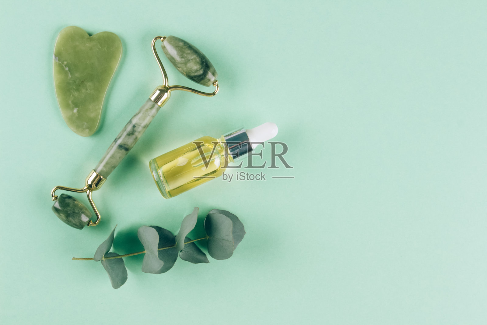 平躺组成与玉瓜沙颜面辊与美血清油粉彩绿色背景与复制空间。由天然石材制成的面部提升按摩疗法包照片摄影图片