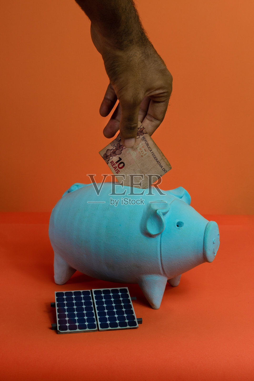 把真正的巴西钱放在小猪里，放在橙色的背景上。太阳能金融形象。照片摄影图片