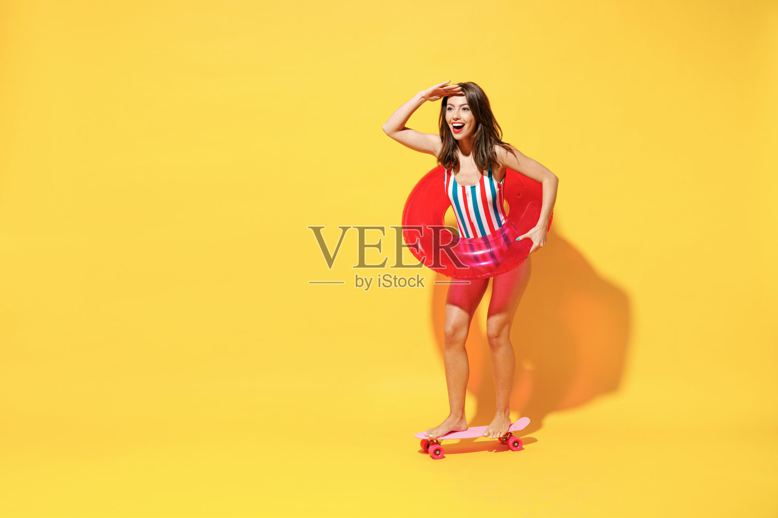 全长快乐年轻性感的女人苗条的身体穿红蓝色泳衣摆姿势与充气环溜冰孤立在生动的黄色墙壁背景工作室。夏季酒店泳池、海景、日光浴的概念。照片摄影图片