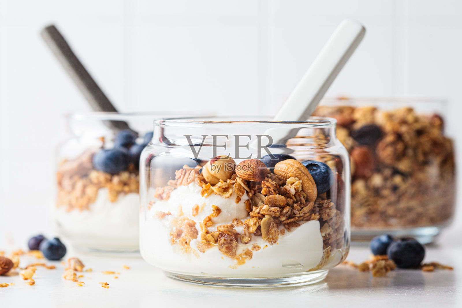 罐装的格兰诺拉麦片，里面有坚果、酸奶和浆果。早餐冻糕，搭配什锦早餐、酸奶和蓝莓，白色底色。照片摄影图片