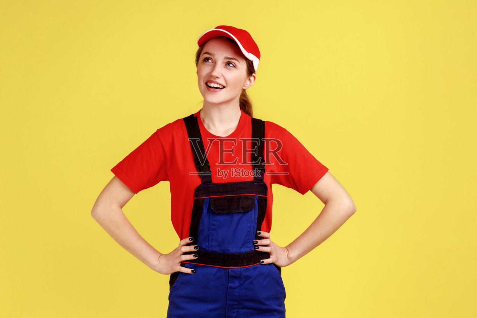 梦幻般的女工站在那里，双手叉腰，望向别处，想着一些愉快的事情。照片摄影图片