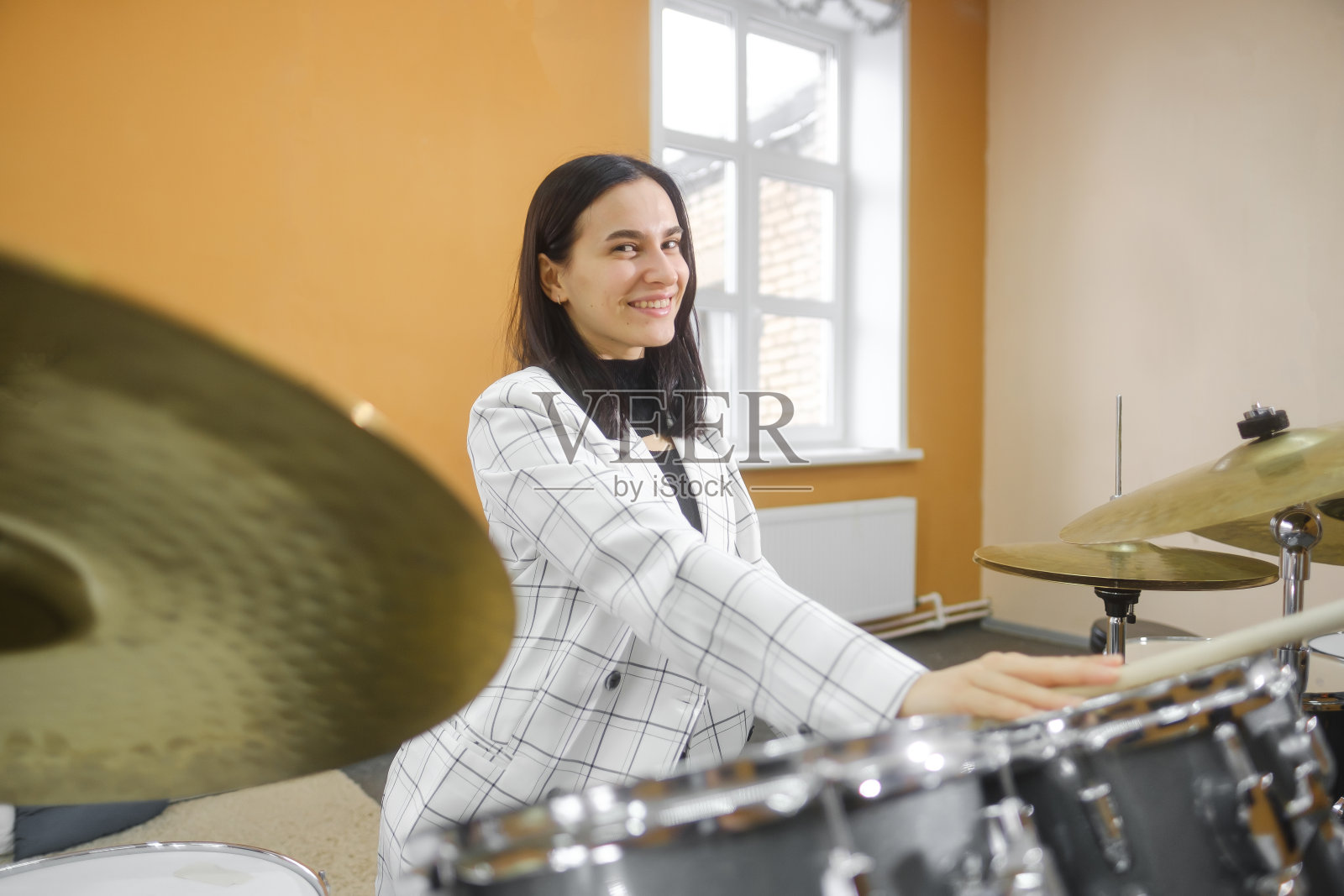 一幅年轻美丽的成年女子的肖像，站在一套鼓后面。爱好和消遣。照片摄影图片