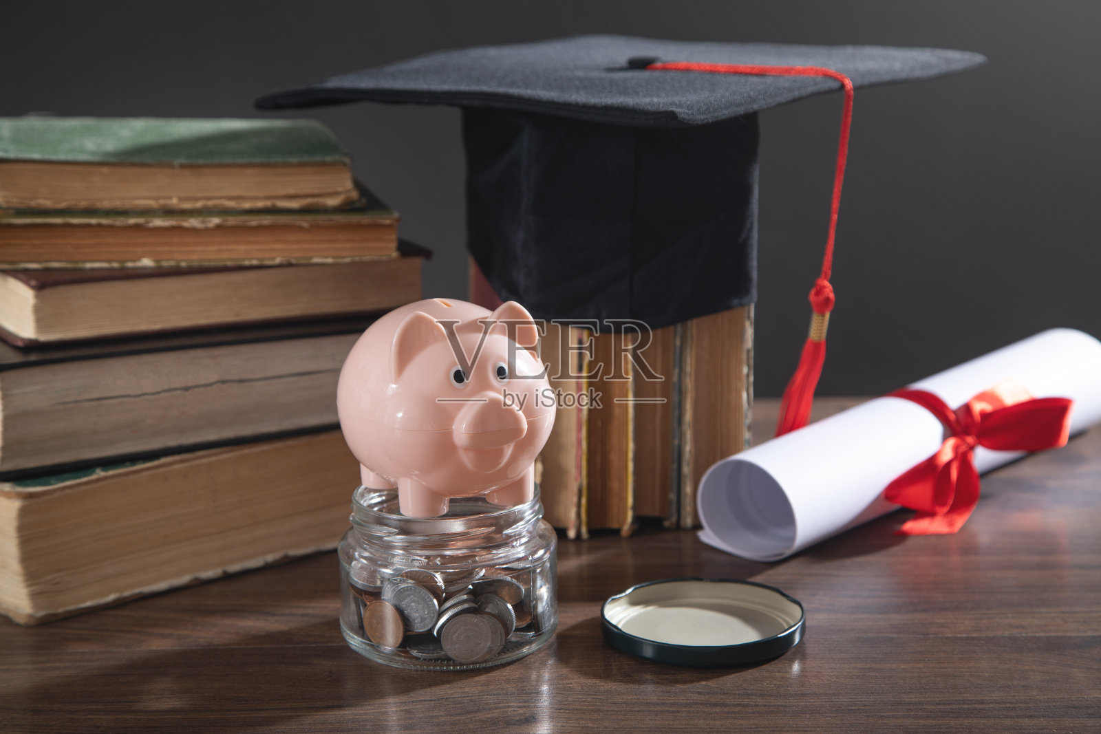 木桌上有毕业帽、书、毕业证书、硬币和储蓄罐。照片摄影图片