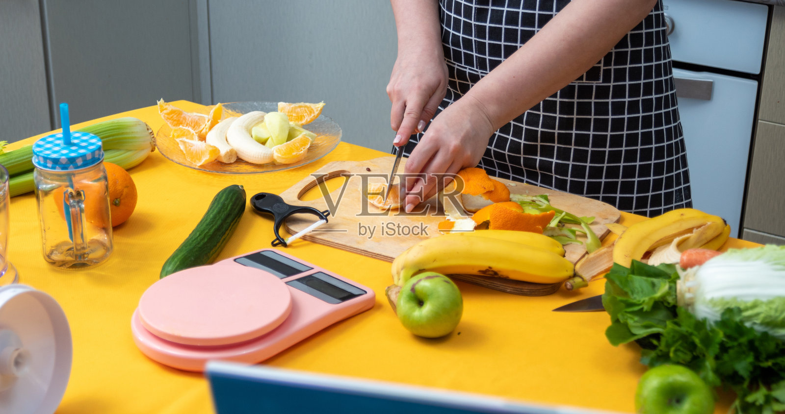 女孩的手正用刀在木板上切橘子。桌子上还有其他制作新鲜奶昔的原料和工具。健康饮食。有选择性的重点。照片摄影图片
