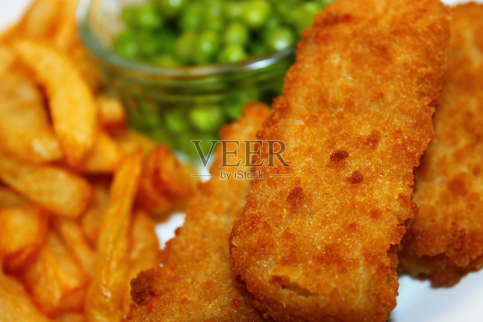 裹着面包屑的黑线鳕片配上大块薯条和豌豆照片摄影图片