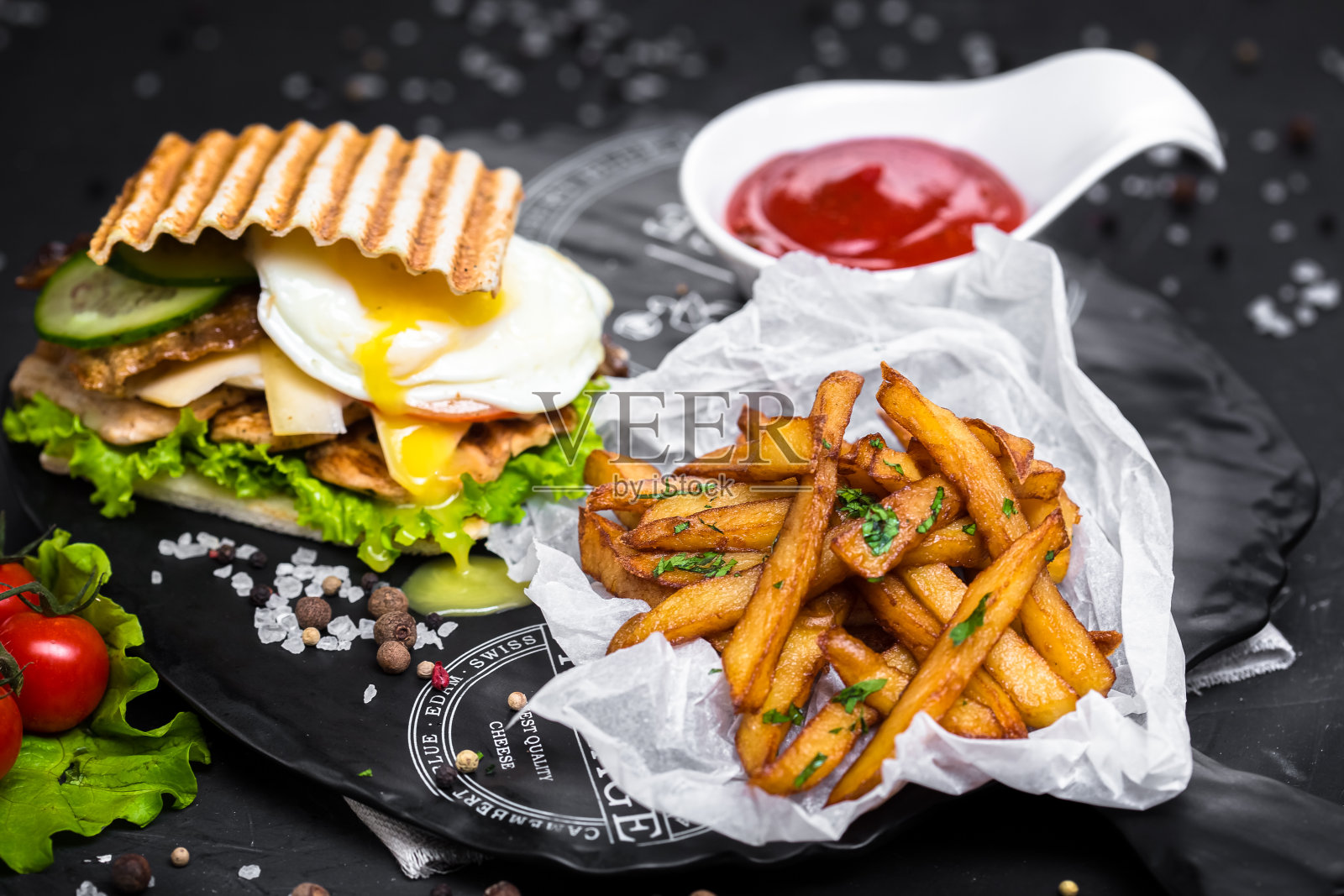 三明治与鸡蛋，肉类和香草，奶酪，油炸薯条或adajo，酱汁在一个白色的碗，一盘蔬菜与布和木板在一个黑色孤立的背景照片摄影图片