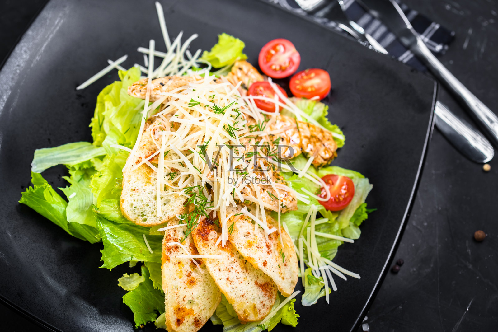 凯撒沙拉配鸡肉块，白色吐司在绿色蔬菜气垫上，奶酪和圣女果，蔬菜布和木板在黑色孤立的背景上照片摄影图片