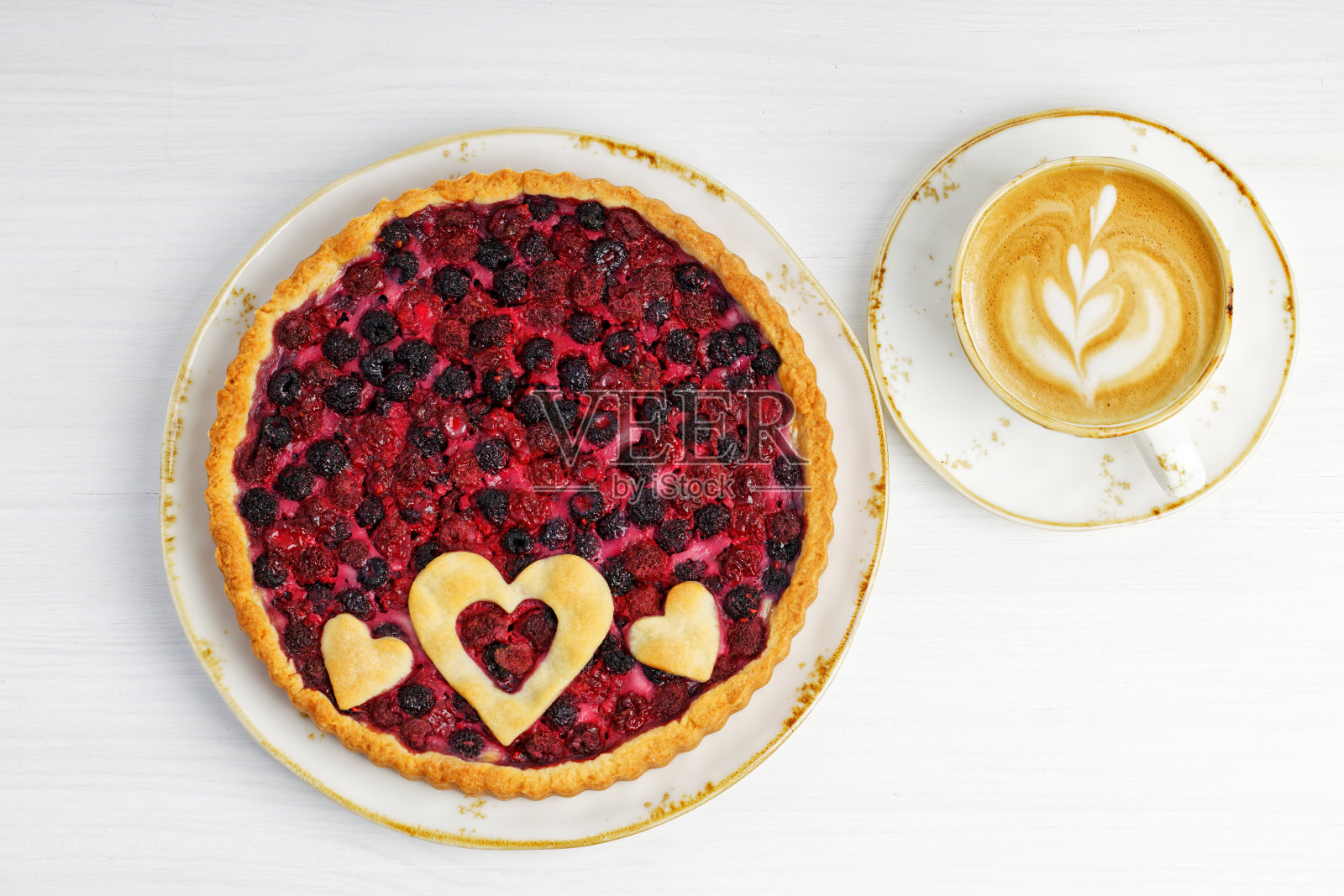 白色木桌上放着自制的开放式派，配上红色和黑色的树莓和一杯卡布奇诺咖啡。前视图。照片摄影图片