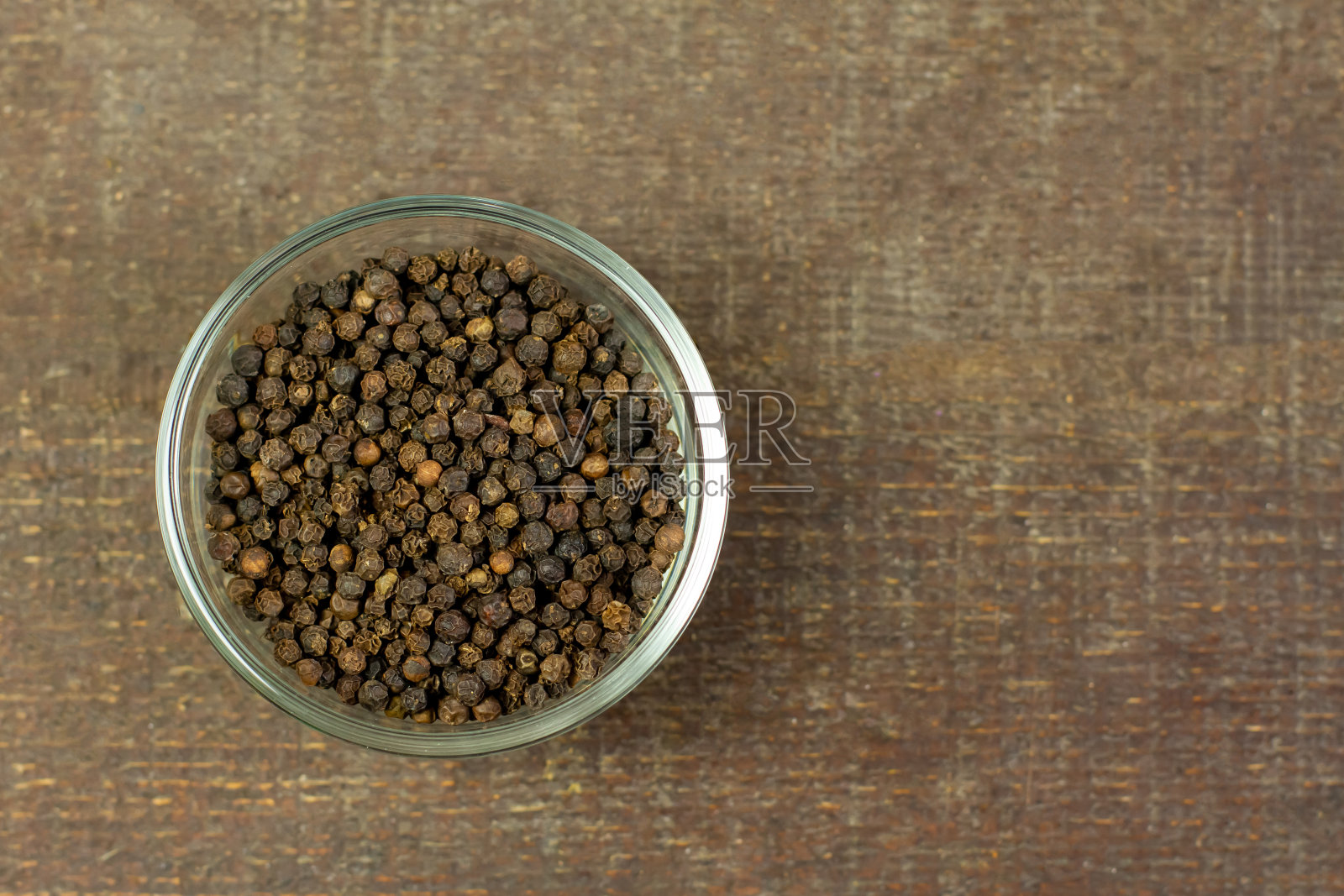 黑胡椒装在棕色木制背景的透明玻璃碗里。照片摄影图片