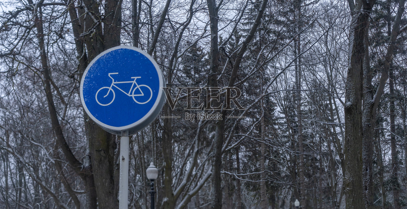冬季公园的蓝色自行车道标志。在寒冷的天气骑自行车。人行道上的自行车模板。交通标志的概念。照片摄影图片