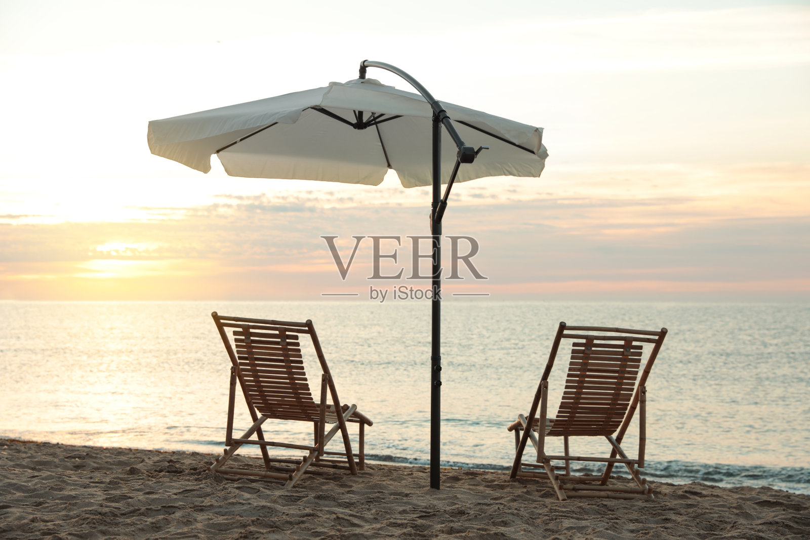 日落时分沙滩上的木制躺椅和户外伞。暑假照片摄影图片