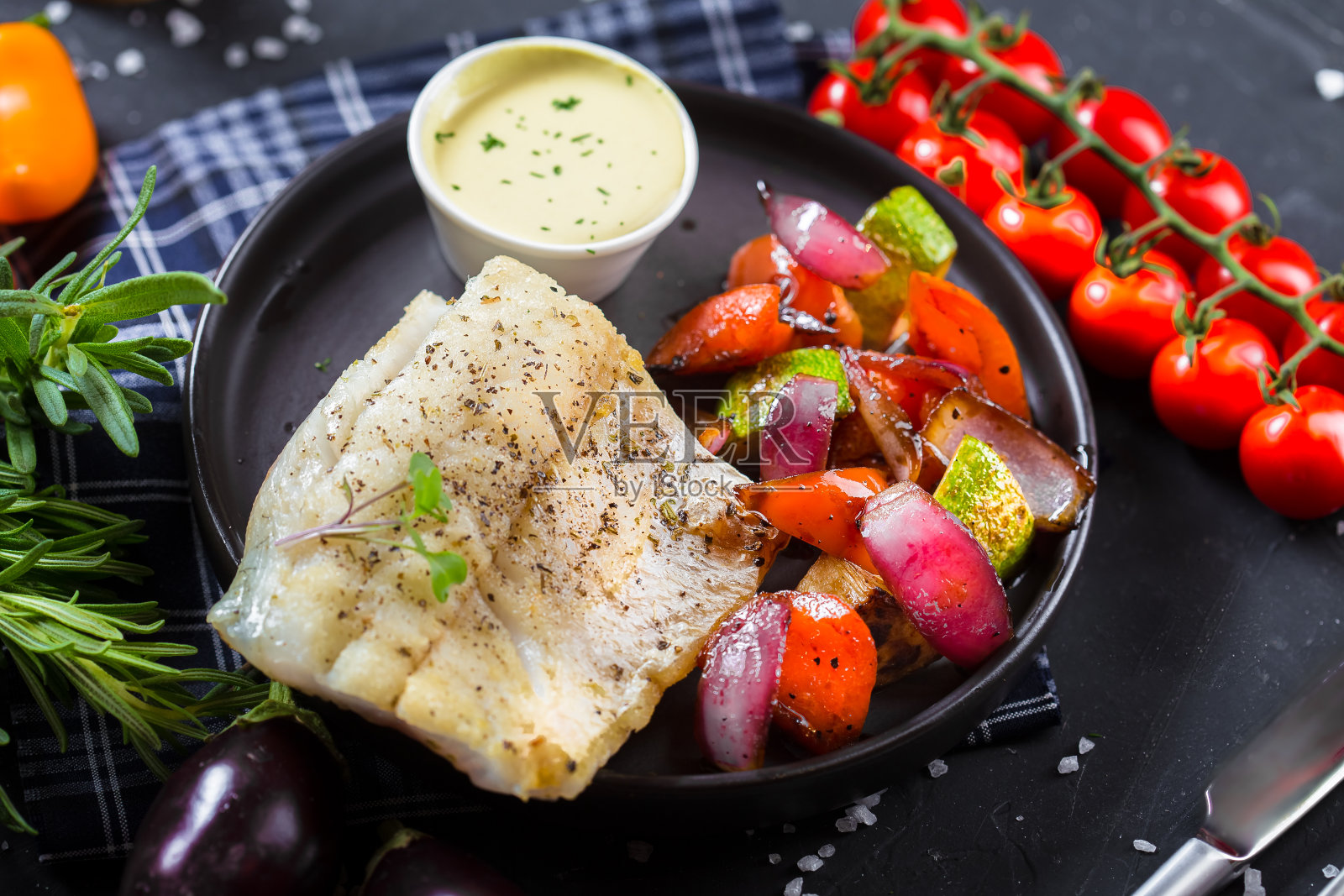 盘子上放着炸鱼排和蔬菜，圣女果，黑色孤立背景的餐具，顶部照片摄影图片