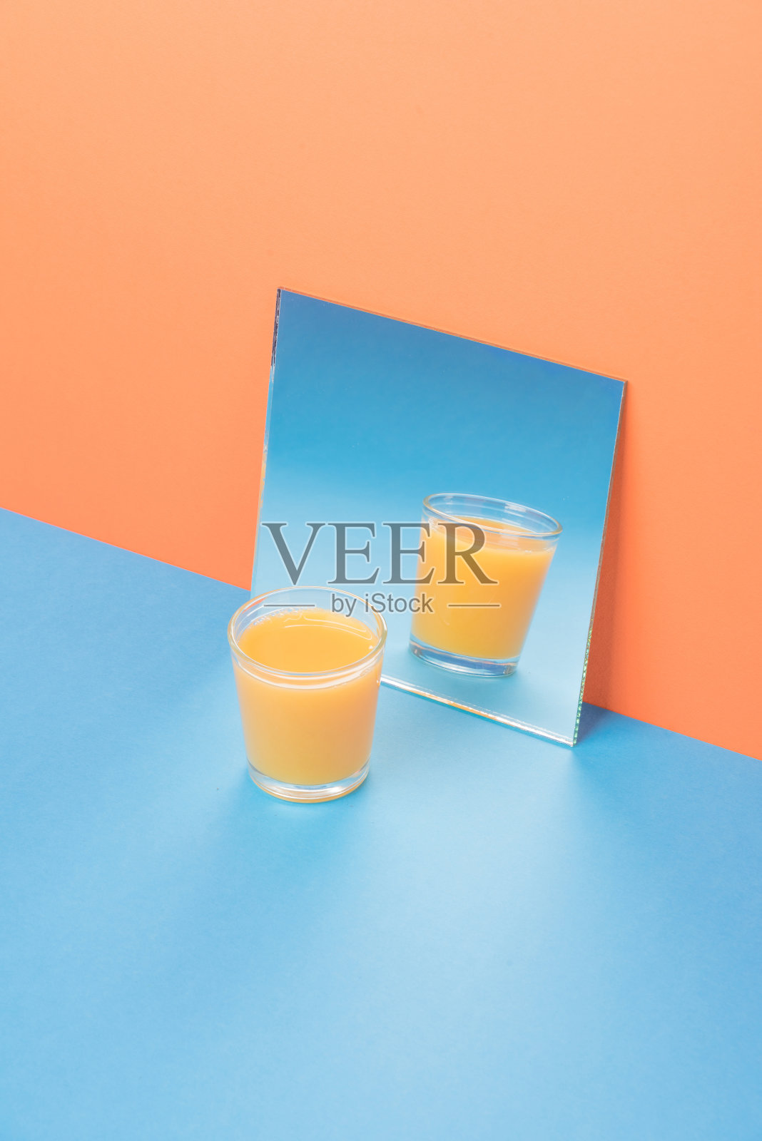 在橙色的背景下，蓝色的桌子上放着一杯果汁。照片摄影图片