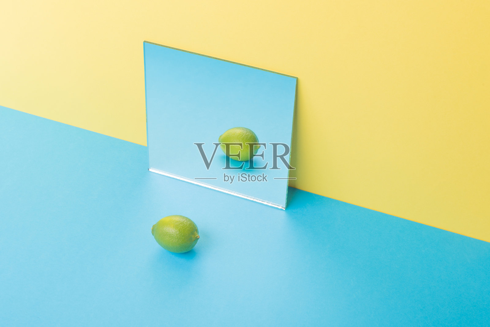 石灰在蓝色的桌子上孤立在黄色的背景上，近镜照片摄影图片