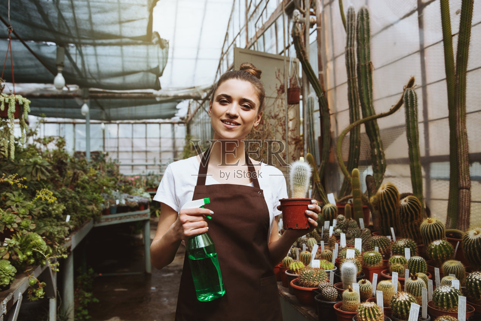 快乐的年轻女子，站在温室里的植物旁边照片摄影图片