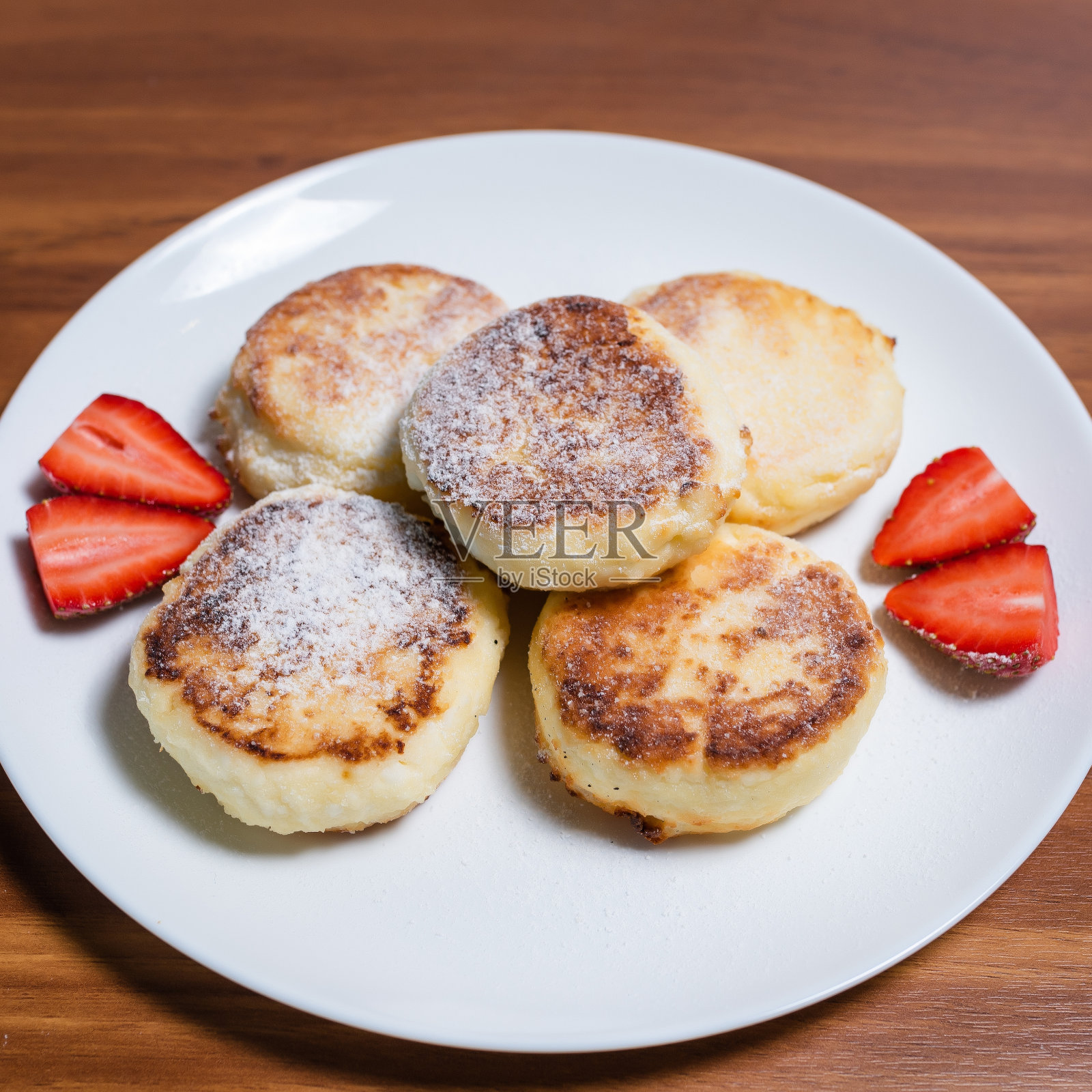 白盘子里的白干酪芝士蛋糕，配粉、奶油、果酱和草莓。健康的早餐。自制的食物照片摄影图片