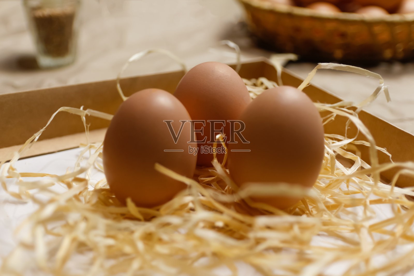 特写镜头三个鸡蛋。复活节工艺盒与棕色鸡蛋在生态背景。用干草和稻草把鸡蛋放在工艺桌上。近距离观察原始产品。木制的稻草。生物和有机照片摄影图片