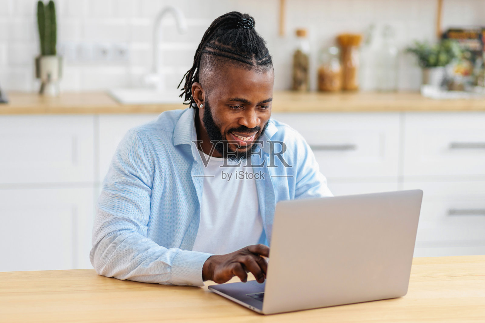 非裔美国男生在家远程学习，在线学习。成功的自由职业者坐在桌子上用笔记本电脑上网工作，笑容亲切照片摄影图片