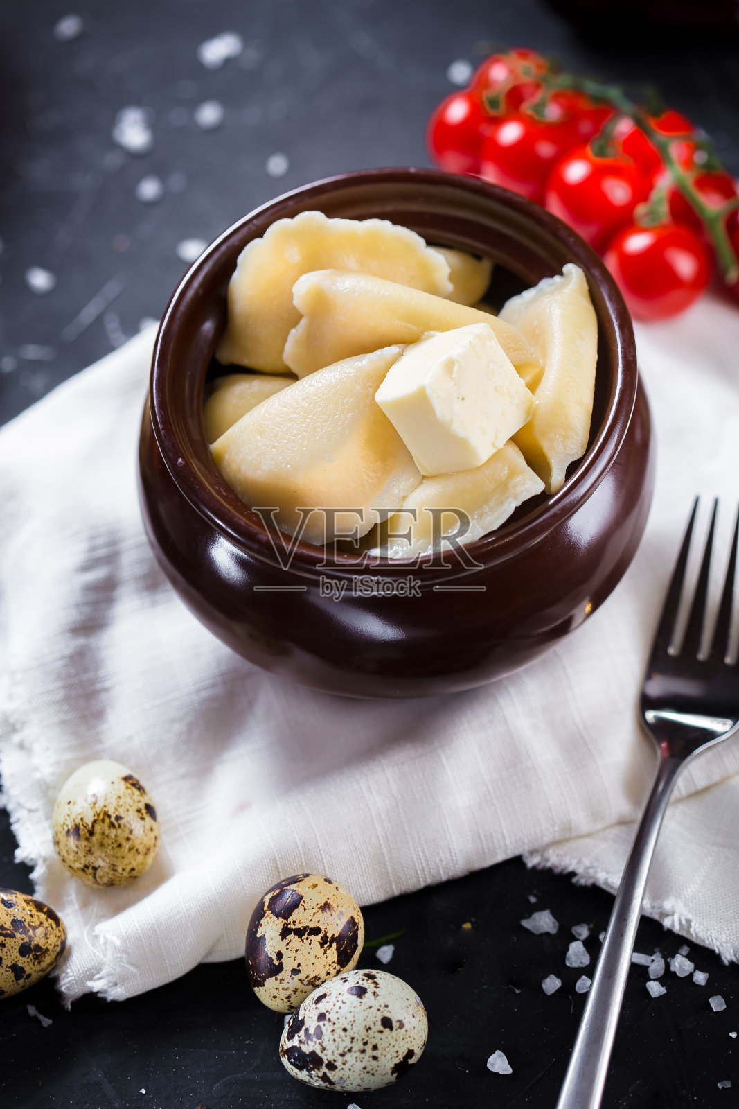 盘子上的饺子配黄油，圣女果，餐具在黑色孤立的背景上，特写，顶部照片摄影图片