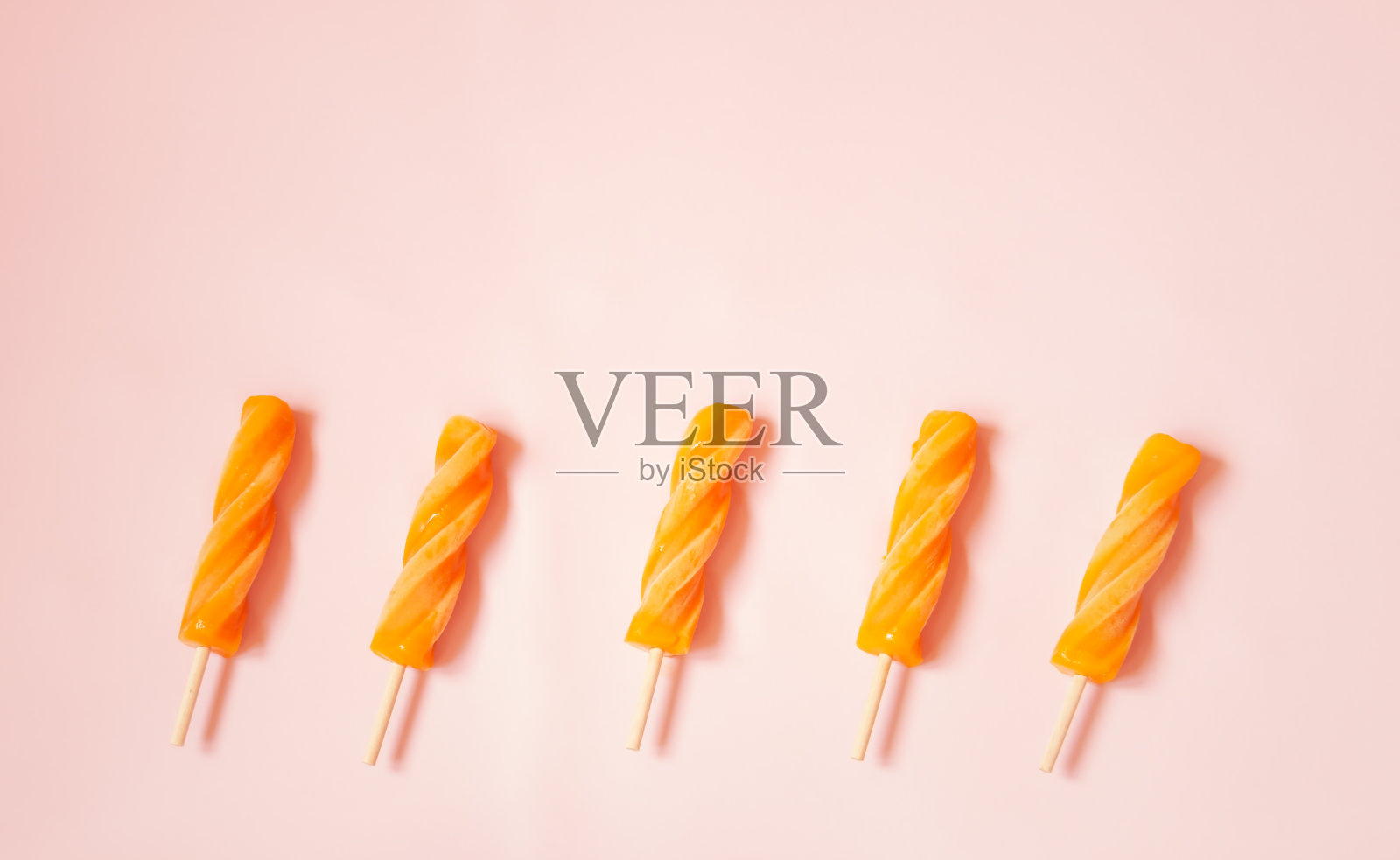 螺旋橙色冰棒作为粉红色背景的边界。照片摄影图片
