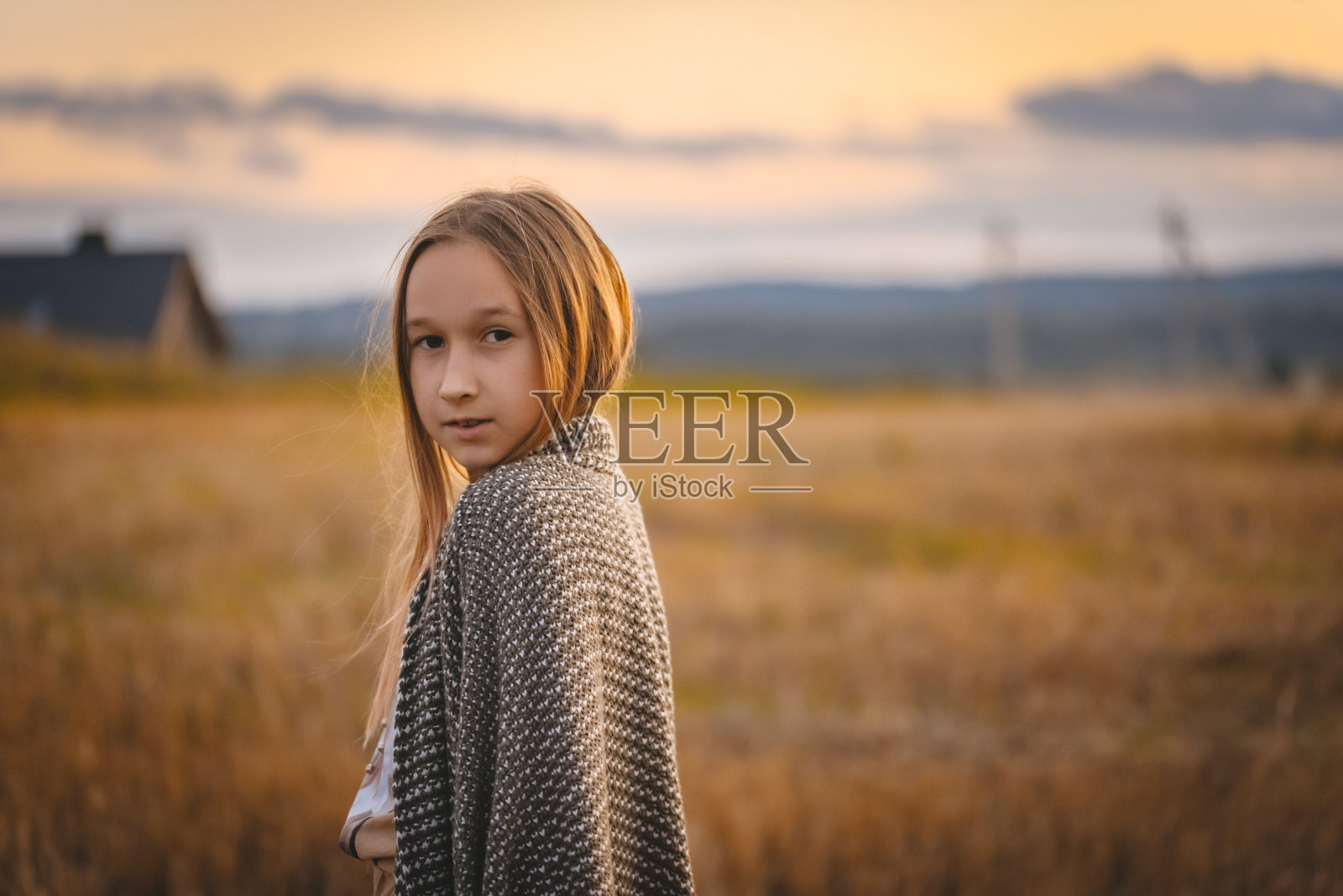 一个孩子裹着毯子在田野里散步。照片摄影图片