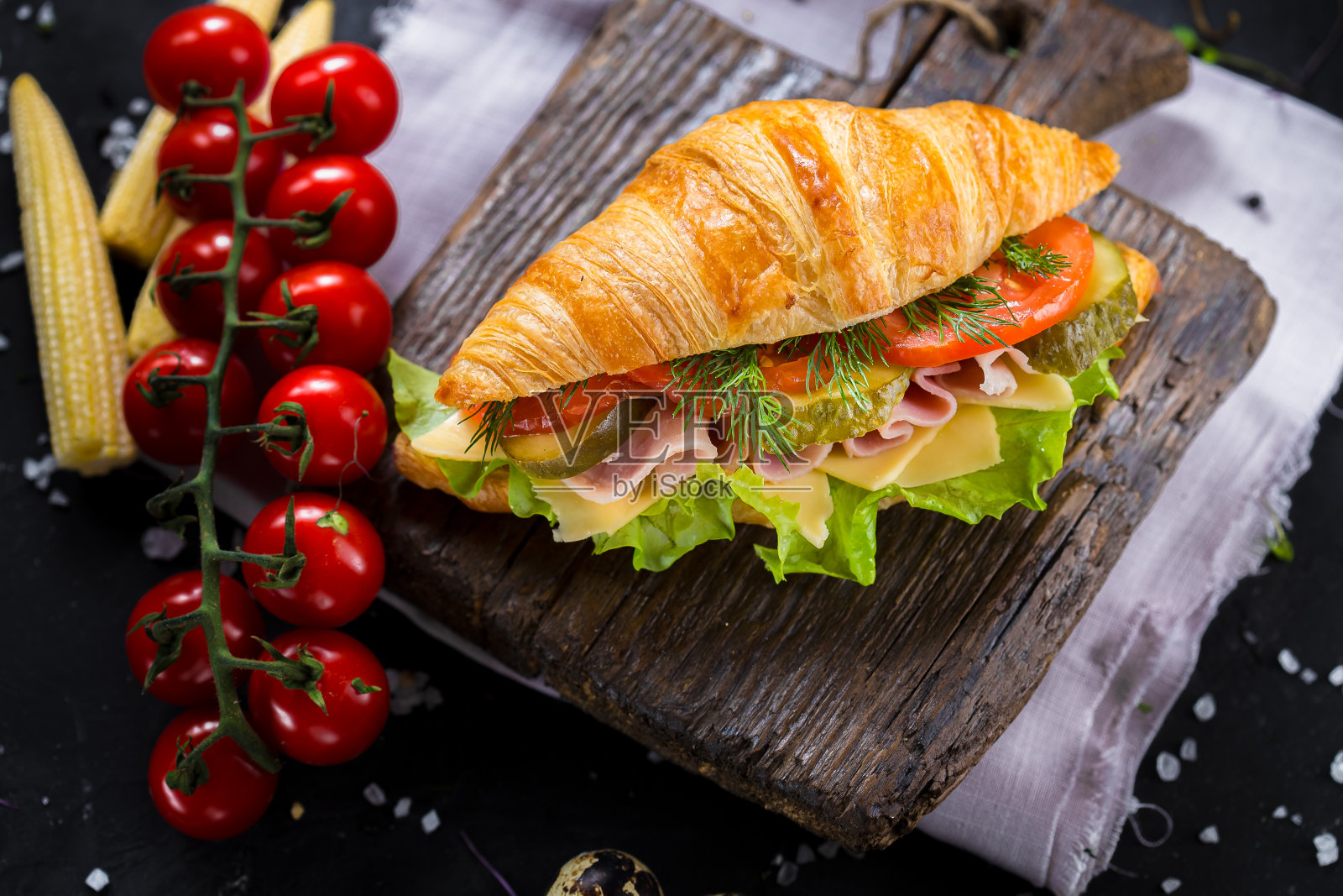 牛角面包与火腿和绿色蔬菜在一个木制切菜板上，蔬菜，圣女果，刀具在一个黑色孤立的背景，顶部照片摄影图片