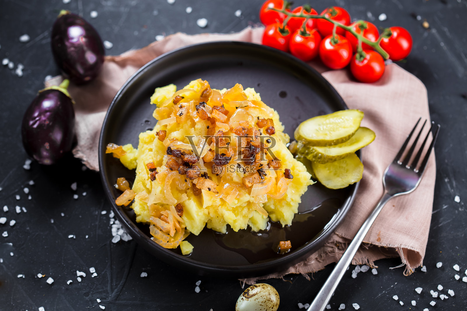 在一个盘子上煮土豆，炸洋葱和培根，洋葱圈和黑面包，樱桃番茄，刀具在一个黑色孤立的背景，顶部照片摄影图片