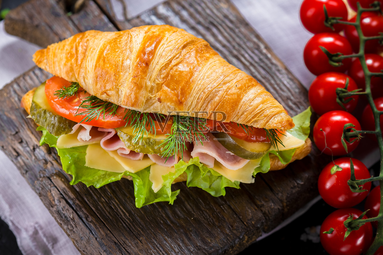 牛角面包与火腿和绿色蔬菜在一个木制切菜板上，蔬菜，圣女果，刀具在一个黑色孤立的背景，顶部照片摄影图片