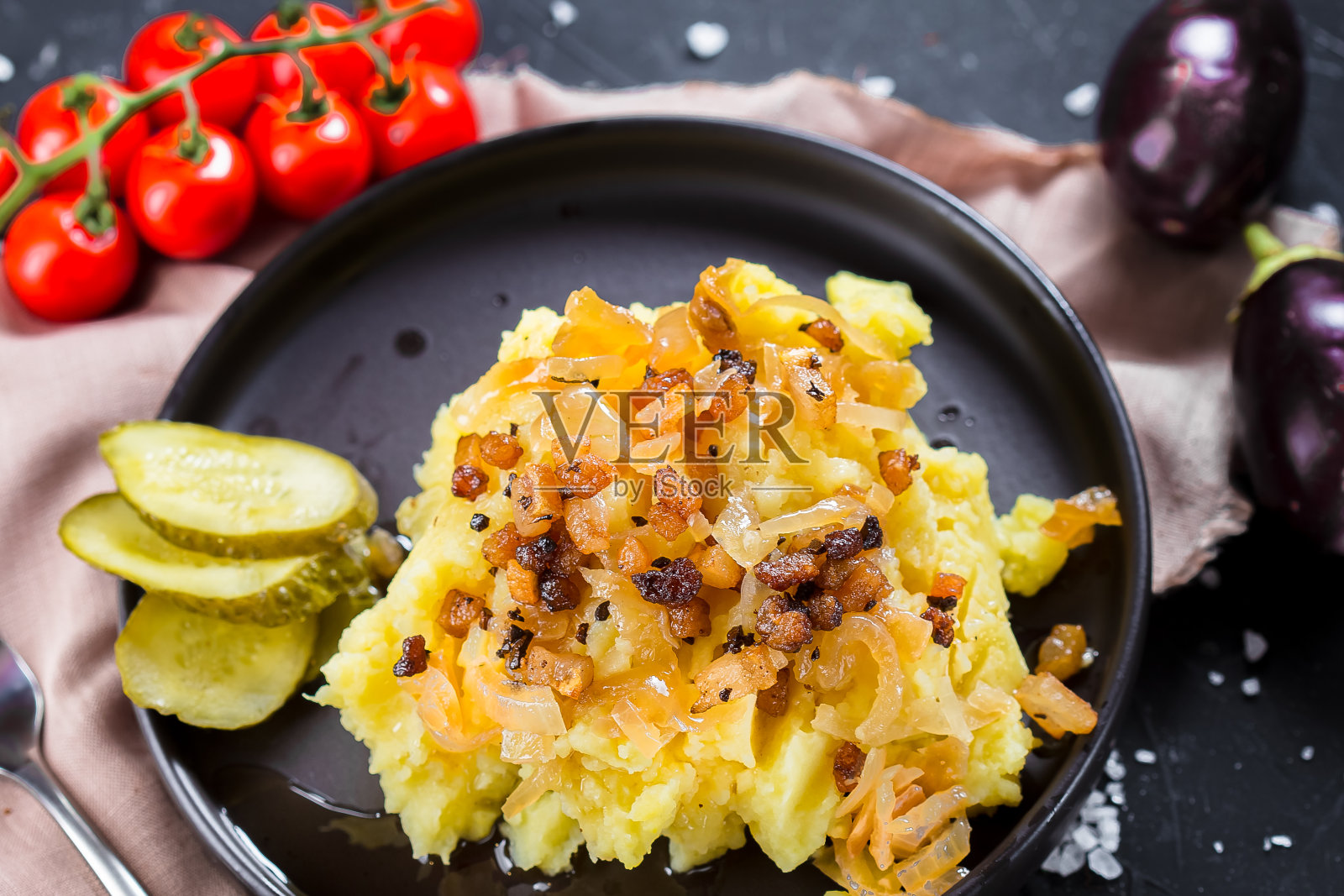 在一个盘子上煮土豆，炸洋葱和培根，洋葱圈和黑面包，樱桃番茄，刀具在一个黑色孤立的背景，顶部照片摄影图片